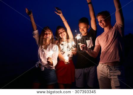 Friends Walking, Dancing And Having Fun During Night Party At The Seaside With Bengal Sparkler Light