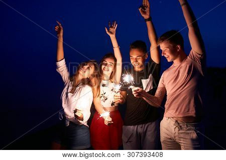 Friends Walking, Dancing And Having Fun During Night Party At The Seaside With Bengal Sparkler Light