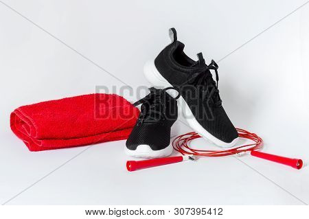 Black Sports Running Shoes With White Sole, Red Jumping Rope And Red Towel Isolated On White Backgro