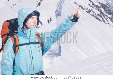 Portrait of adventurous young man on winter mountainside view pointing out. Snowboarders walking uphill for freeride, extreme sport. Active lifestyle and tourism.