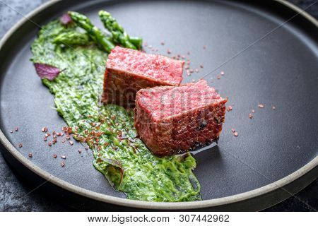 Blanched green asparagus tips with barbecue dry aged wagyu fillet steak and avocado coriander relish as closeup on a modern design plate