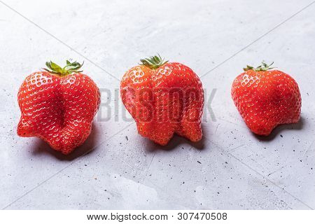 Close-up Three Ugly  Red Strawberries On Concrete Background.