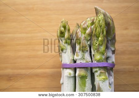 Bunch Of Frozen Wild Asparagus Tied With Rubber Tape From Ecological Agricuture Over Wooden Backgrou