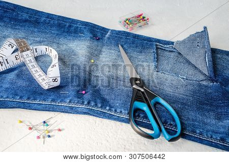 Folded In Half Blue Jeans With Large Hole On Pant Leg Below The Knee, Multi Coloured Headed Sewing P