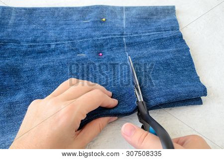 Woman Hand Holding A Scissors And Cutting Blue Denim Shorts To Make Them Shorter. Making Jeans Short