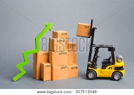 Yellow Forklift Truckraises A Box Over A Stack Of Boxes And A Green Arrow Up. High Trade Volumes, In
