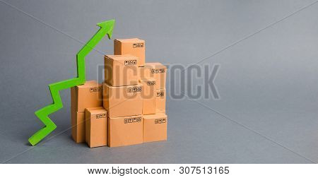Lots Of Cardboard Boxes And A Green Arrow Up. Growth Rate Of Production Goods, Raise Economic Indica