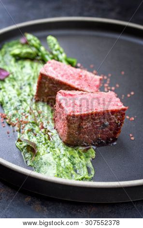 Blanched green asparagus tips with barbecue dry aged wagyu fillet steak and avocado coriander relish as closeup on a modern design plate