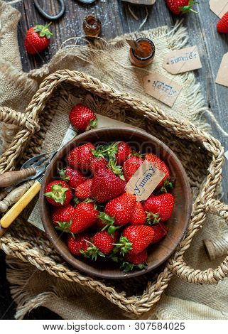Overhead Shot Of Tasty Ripe Strawberries In Wooden Bowl Stands In Wicker Strawy Basket On Rustic Tab
