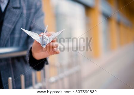 Young Woman Playing Origami Birds, White Cranes In Hands Against Sky Reflection In A Window