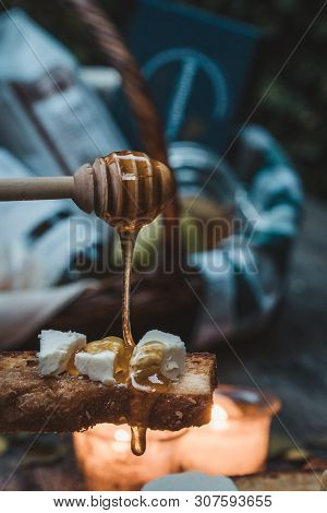 Honey Dripping Over A Bread With Cheese Backlit By Candles