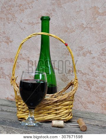 Still Life With An Open Bottle Of Red Wine, A Glass And A Basket.