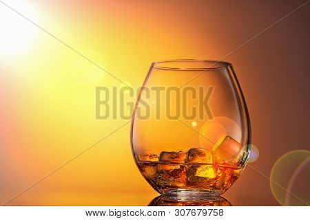Glass Of Whiskey Scotch With Ice On An Orange Background, It Is Illuminated By Sunlight. Close Up, C
