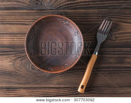 Clay Bowl On A Brown Wooden Table. Pottery For The Kitchen. The View From The Top. Flat Lay.
