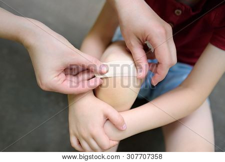 Mother Hands Applying Antibacterial Medical Adhesive Plaster On Child's Knee After Falling Down.