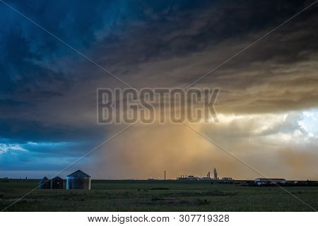 A Powerful Storm Blows Dust Clouds Over Farmland With The Setting Sun Illuminating The Scene.