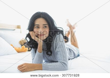 Close Up Shot Of Lovely Asian Woman Smiles, Prop Up And Lie Prone On The Bed In Bedroom.