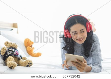 Close Up Shot Of Lovely Asian Woman Lie Prone, Prop Up, Smiles And Wearing Headphone That Connect To