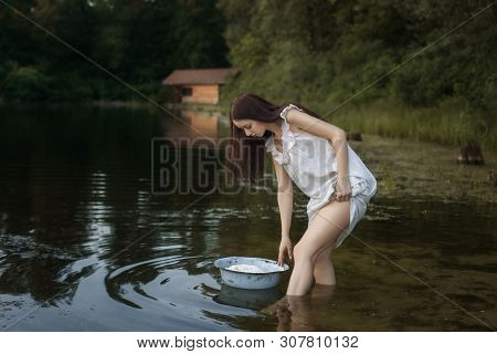 Young Laundress Stands In The River, In Front Of Her Is A Basin Of Linen. She Is Preparing To Wash.