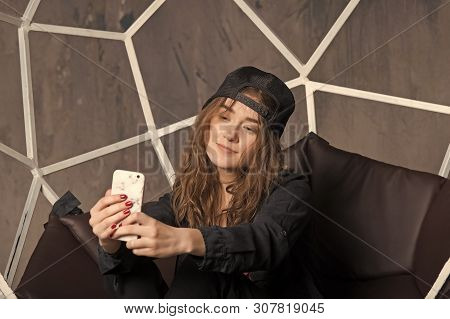 Girl Or Woman In Baseball Cap Making Selfie With Smartphone On Brown Chair. Technology And Mobile De