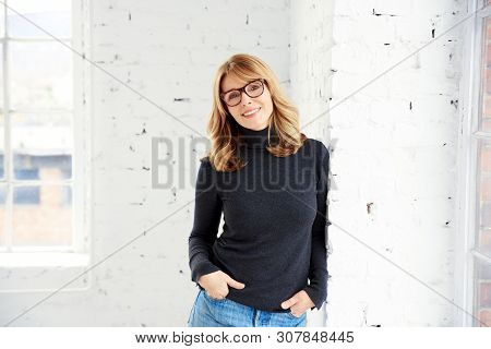 Portrait Of Attractive Woman Wearing Roll Neck Sweater And Jeans While Looking At Camera And Smiling