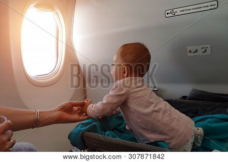 Happy Infant Baby Lyes In Special Bassinet In Airplane At His Stomach. First Flight Of The Baby, She