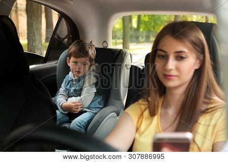 Mother Using Phone While Driving Car With Her Son On Backseat. Child In Danger