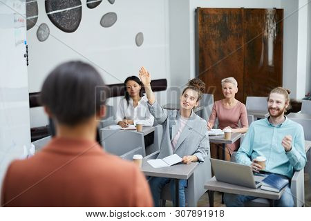 Wide Angle Portrait Of Contemporary Young Woman Raising Hand In Class With Group Of Student Enjoying