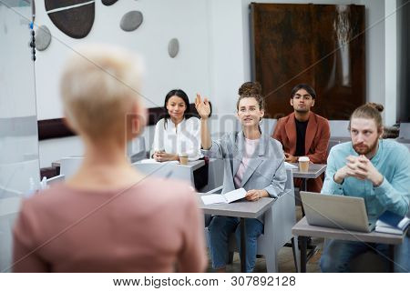 Wide Angle Portrait Of Contemporary Young Woman Raising Hand In Class With Group Of Student Enjoying