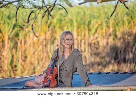 Smiling Happy Woman Holding Her Rare French Antique Violin Sitting On A Trampoline With Late Afterno
