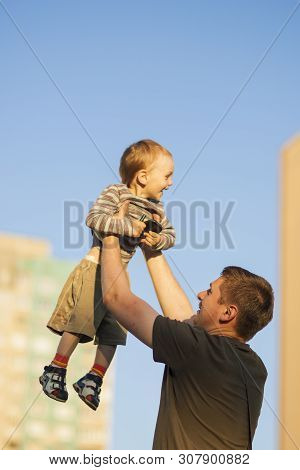 Father And Happy Son Playing Together Outdoors.dad Tossing Son Up Against Blue Sky.  Vertcal Orienta