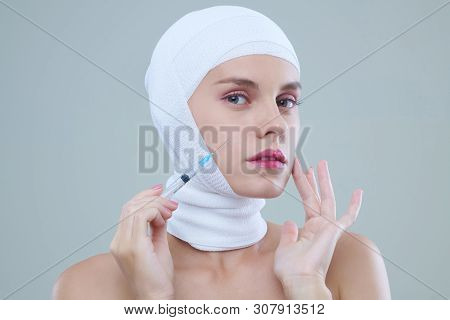 Portrait Of Beauty Victim With Head Bandage Holding Syringe With Filler