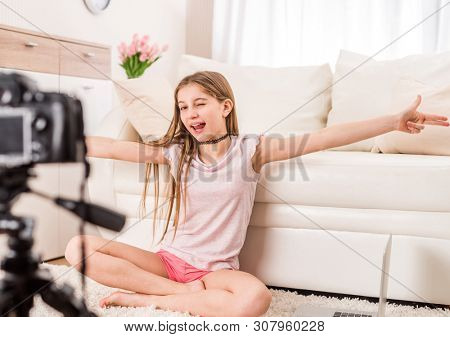 Young smiling videobloger teen girl is pointing at camera in living room