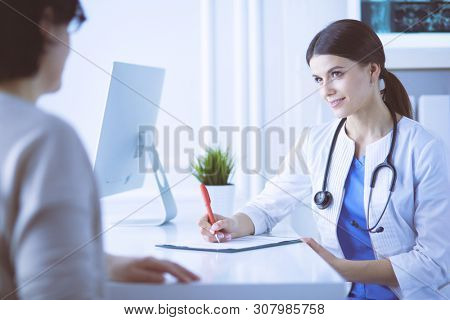 Doctor and patient discussing medical problems in a hospital consulting room. Doc filling in a patient's form