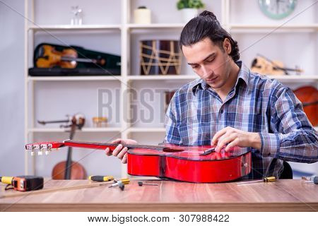 Young handsome repairman repairing guitar