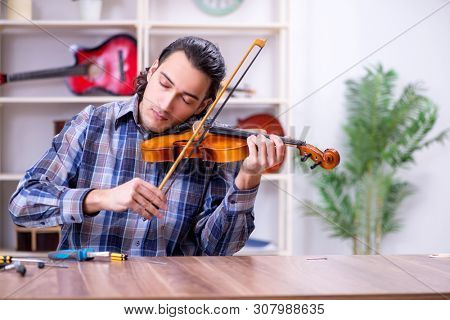Young handsome repairman repairing violin
