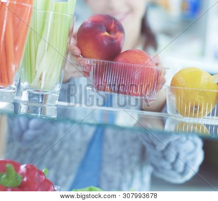 Portrait of female standing near open fridge full of healthy food, vegetables and fruits. Portrait of female