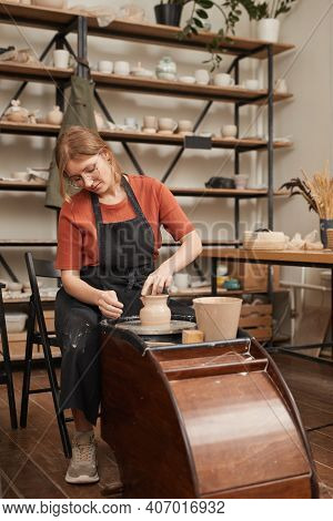 Vertical Warm Toned Portrait Of Young Female Potter Shaping Clay On Pottery Whee While Making Cerami