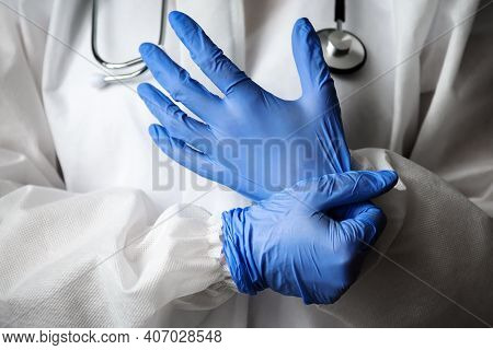 Doctor In Medical Ppe Suit With Stethoscope Close-up, Doctor Puts On Blue Protective Gloves In Hospi