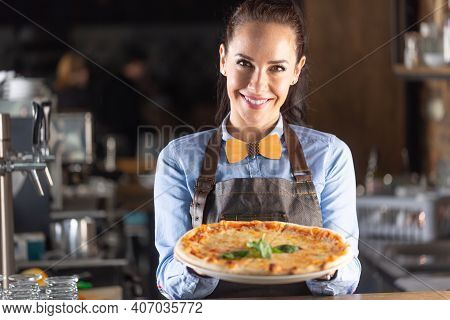 Waitress Smiles While Serving Large Authentic Italian Pizza In A Restaurant.