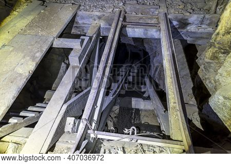 Looking Down A Mine Shaft That Contains A Wooden Ladder And Goes Deep Below The Ground