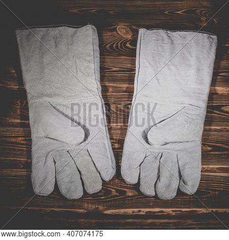 White Leather Welder Gloves On A Wooden Background. A Studio Photo With Hard Lighting.
