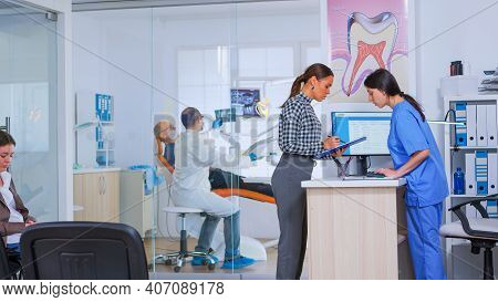 Professional Dentist Asking Nurse For Dental X-ray Before Examining Patient While People Waiting In 