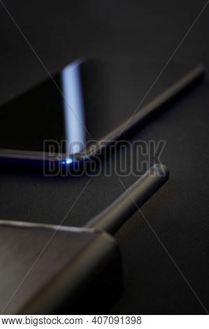 The Antenna Of A Black Router And A Smartphone With Blue Labels Lie On A Dark Background. Wireless T