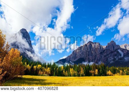 The city of Canmore is surrounded by the majestic Rocky Mountains. The Three Sisters Mountain is covered in lush white clouds.  The concept of active, ecological and photo tourism
