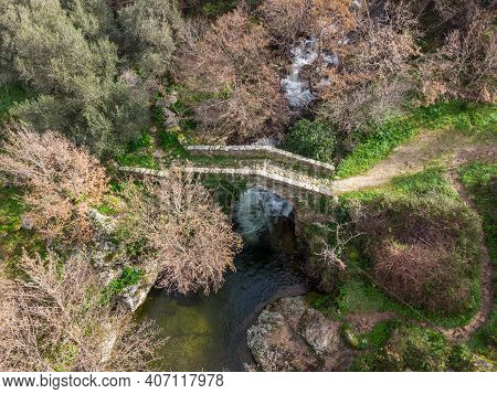 Aerial View Of A Mountain Stream Rushing Through A Woodland And Cascading Beneath An Ancient Genoese