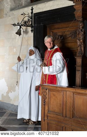 Nun ringing a bell at the beginning of catholic mass in a medieval church