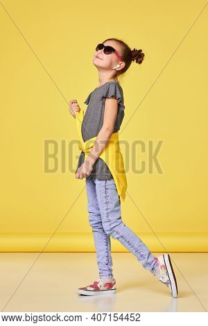 Fashionable Little Child Girl In Sunglasses Posing On Yellow Studio Background. Full Lenth