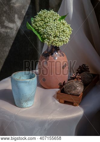 Blue Ceramic Mug Handmade With Bunch Of Flowers In Vase And Dried Cerbera Oddloam's On White Table I