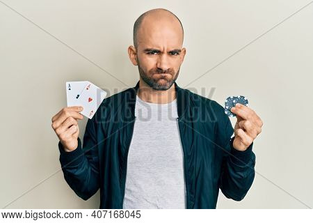 Young hispanic man playing poker holding casino cards and chips skeptic and nervous, frowning upset because of problem. negative person. 